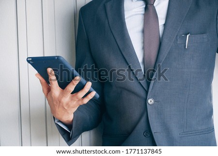 Close up businessman wear suit which have necktie standing and watching tablet on right hand near the wall in the office. 