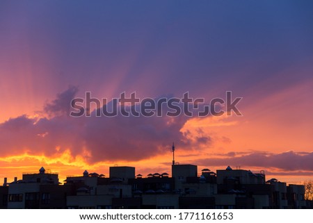 Pink orange purple sunset over the city. Multicolored sky and black silhouette of tall buildings of the metropolis. Big cloud and sun rays
