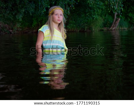 blonde girls with blue eyes bathes in clothes in the dark water of a lake at sunset