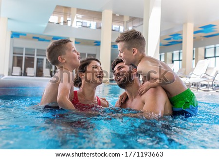 Smiling family of four having fun and relaxing in indoor swimming pool at hotel resort. Royalty-Free Stock Photo #1771193663