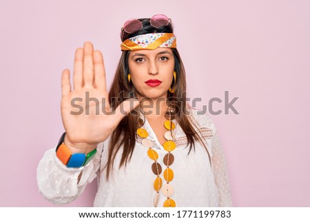 Young hispanic hippie woman wearing fashion boho style and sunglasses over pink background doing stop sing with palm of the hand. Warning expression with negative and serious gesture on the face.