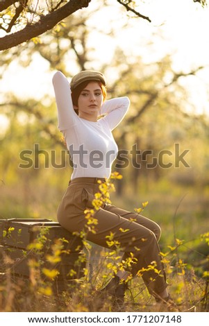  young beautiful red hair stylish  girl  seating on the boxes in apple  tree garden, pants and white turtleneck, natural background