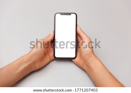 Close-up of a smartphone with a white screen in female hands. Mobile phone on table background