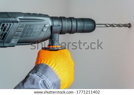  workman hand with a rotary hammer. Hands in protective gloves with hammer drill perforator. close-up Royalty-Free Stock Photo #1771211402