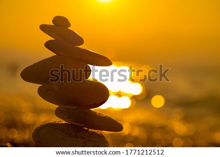 Balanced Pebbles Pyramid on the Beach on Sunny Day and Clear Sky at Sunset. Blue Sea on Background Selective focus, zen stones on sea beach, meditation, spa, harmony, calm, balance concept
