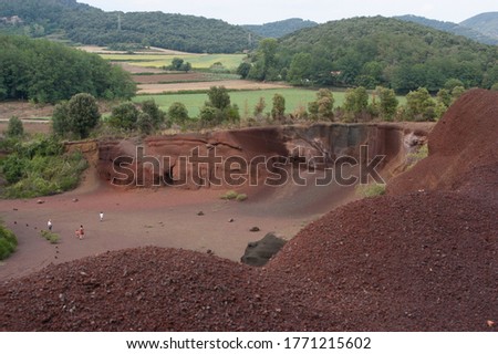 Crater of the Croscat volcano in Catalonia, close-uppart of the top that frames the bottom with people walking through it. In the background vegetation and cultivated fields.