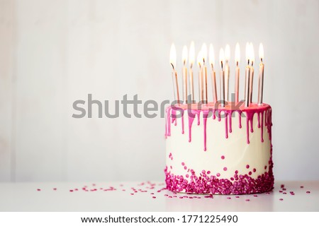 Birthday cake with pink drip icing and birthday candles with copy space to side
