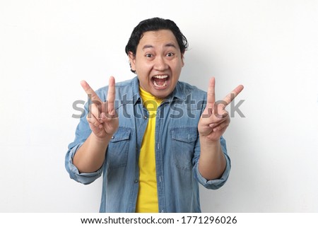 Portrait of good looking  young Asian man shows number two or peace sign gesture with his finger against white wall