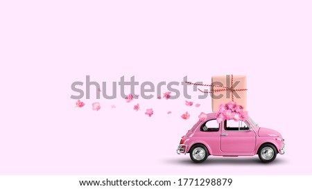 Pink retro car with gift box on a roof with flowers on pink background. Royalty-Free Stock Photo #1771298879