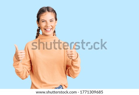 Beautiful caucasian woman with blonde hair wearing casual winter sweater success sign doing positive gesture with hand, thumbs up smiling and happy. cheerful expression and winner gesture. 