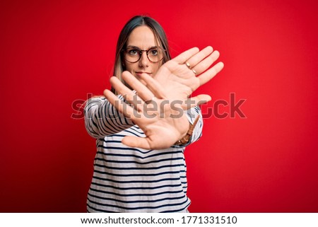Young beautiful blonde woman with blue eyes wearing glasses standing over red background Rejection expression crossing arms and palms doing negative sign, angry face
