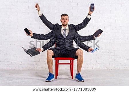 A man with many hands sits on a chair in a jacket and shorts. Multitasking. Business man, workaholic. Royalty-Free Stock Photo #1771383089