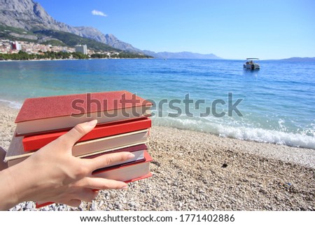 A young pretty girl holds books in her hands on the beach by the sea