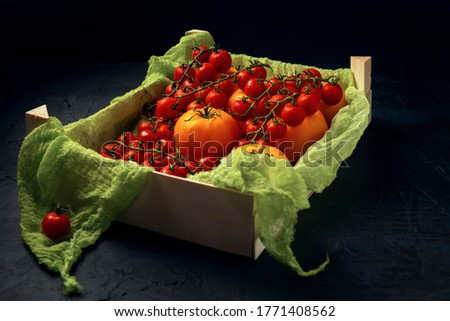 A wooden box with red cherry tomatoes and ripe yellow tomato fruits on dark textured table.