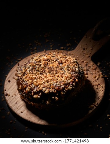 A vertical picture of a chocolate cake with nuts against a black background