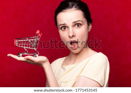 woman shows the economy on the example of an empty toy trolley from the supermarket, red background