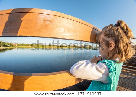 Little girl looking at the pond on top of the pier on a sunny afternoon.
