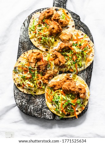 Deep fried fish and coleslaw salad tacos on a cutting board on light background, top view