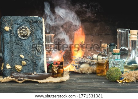 Magic potion and spell book on the table on burning fire in fireplace background. The Witchcraft.