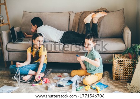Daytime with family at home. Mother working from home, using laptop. Children playing games on a tablet and watching cartoons.