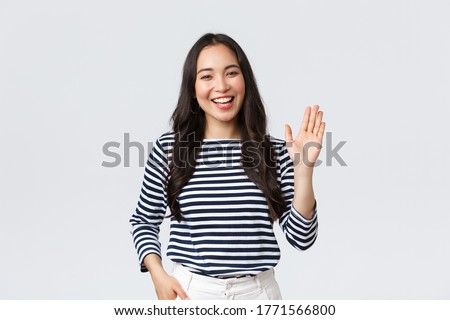 Lifestyle, people emotions and casual concept. Friendly cheerful asian woman smiling, saying hi and waving hand to greet person, make hello gesture, welcome someone Royalty-Free Stock Photo #1771566800