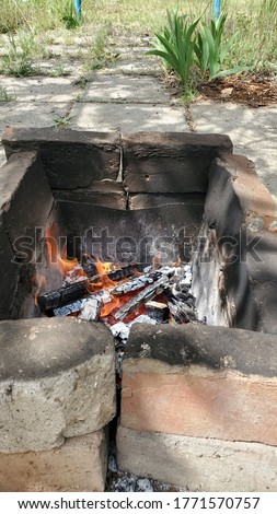 Rustic mangal made from cracked burnt red bricks with smoky surface. Burning fire inside old brazier with smoldering firewood. Bonfire flames in outdoor mangal