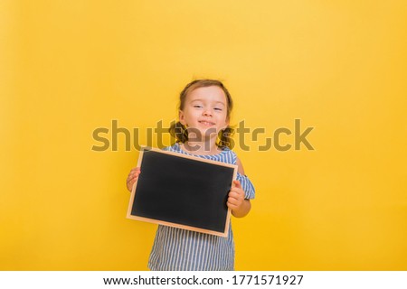 A happy little girl holds an empty slate on a yellow isolated background with space for text
