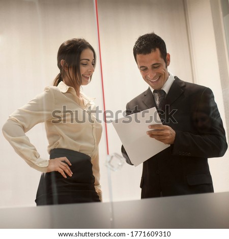 couple of elegantly dressed business colleagues discuss standing in a windowed office