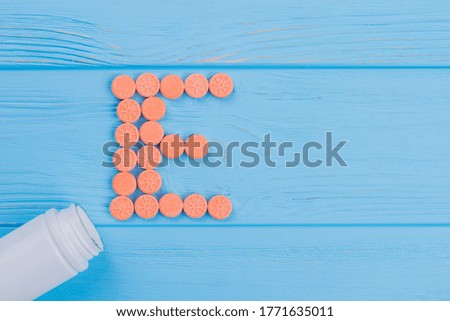 Letter E made of round tablet pills. Blue wooden background.