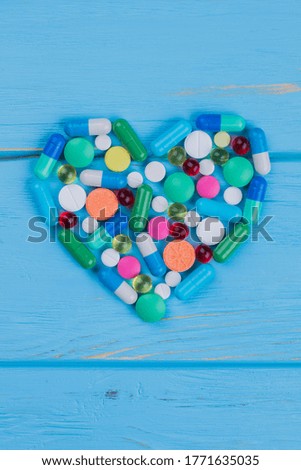 Various medicine pills on a shape of heart. Blue wooden background.