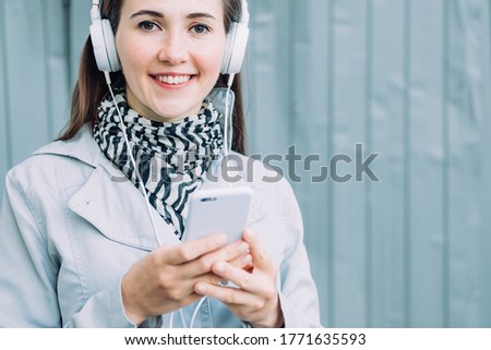Caucasian girl in headphones smiling and looking at the camera while listening to music.