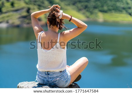 girl in short jeans, cap and sweatshirt enjoying the view of a mountain lake on vacation.