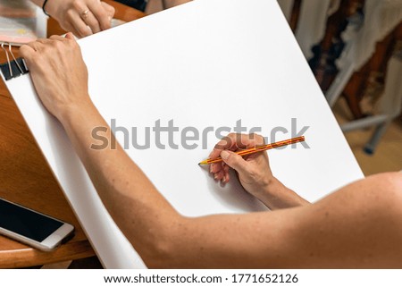 Female hand holding a wooden pencil ready to draw a sketch paint on a white paper.