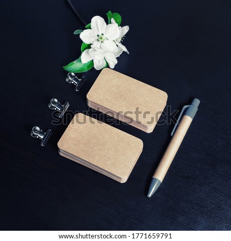 Blank kraft paper business cards, pen and flowers on black wooden background. ID template. Mock-up for branding identity for designers.