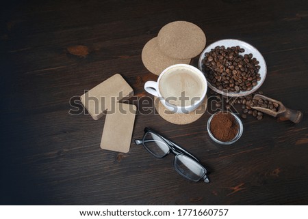 Still life with coffee cup, coffee beans, ground powder, beer coasters, blank kraft business cards and glasses on wooden background. Top view. Flat lay.