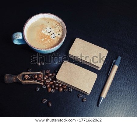 Blank kraft business cards, coffee cup, pen and coffee beans on black wooden background. Template for graphic designers portfolios.