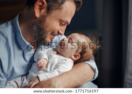 Closeup portrait of middle age bearded Caucasian father hugging and kissing newborn baby. Male man parent holding child. Authentic lifestyle touching tender moment. Single dad family life concept.  Royalty-Free Stock Photo #1771716197