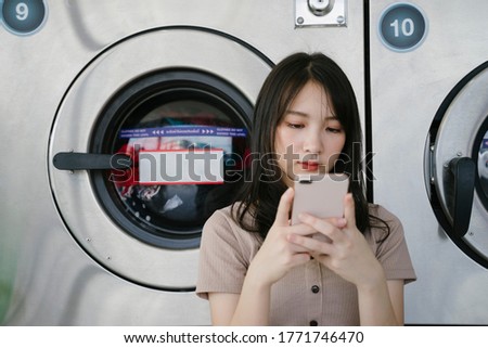 Long air girl use smartphone in front of washing machine.
