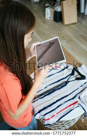 Long hair woman take a photo of the stripped shirt, her goods, then send the photo to the customer to make sure about the quality.