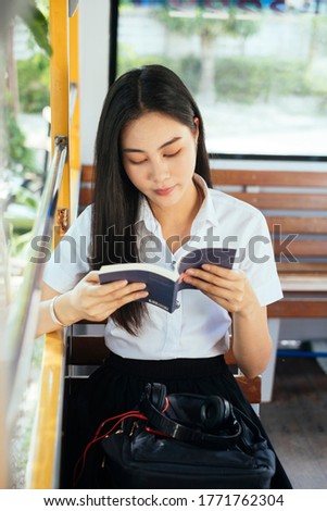 Black long hair college girl in uniform sitting on the empty bus reading the book, vertical.