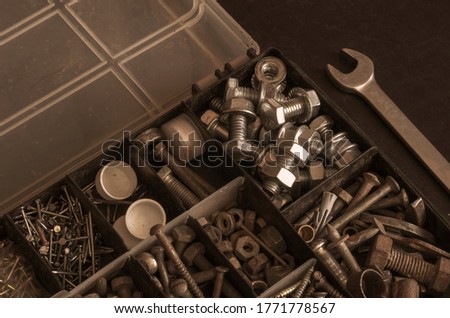 Plastic box with a variety of metal fasteners. Old and new bolts, nuts, screws and screws. Industrial background with copy space. Tinted photo. Selective focus.