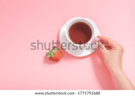woman's hand with a Cup of tea and a strawberry berry on a pink background. top view. copyspace