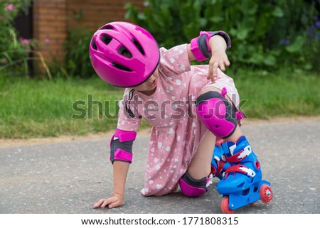 A little girl roller skating in full protection fell on the asphalt. The concept of an active healthy lifestyle and safe riding.