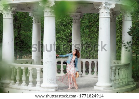 A slender girl stands in a white gazebo located in a summer Park. Image with selective focus, noise effects.