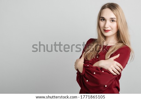 Love, care tenderness concept. Charming European young woman with long blonde hair standing, crossing arms on her chest, on gray background. Copy space for your text
