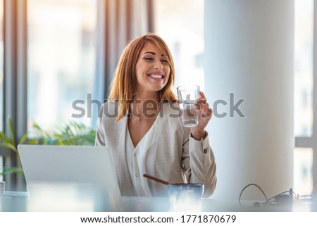Businesswoman drinking water while working in her office. Close up of woman using a computer while holding a glass of water. Dehydrated female office worker drinking still mineral water 