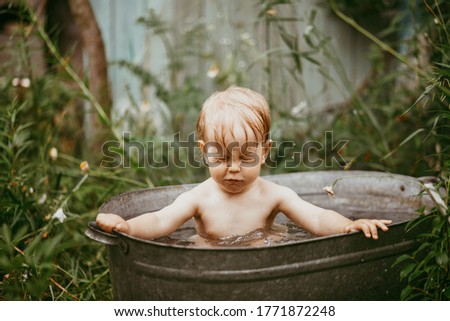 a little boy bathes in a basin in the summer in a green garden.