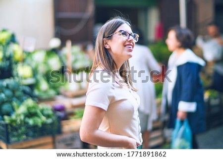 Young beautiful woman smiling happy and confident. Standing with smile on face looking at greengrocery at the town street