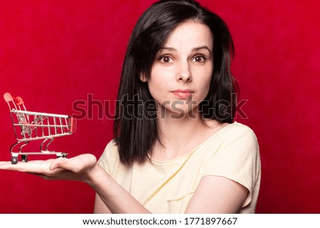 woman in yellow t-shirt holding supermarket trolley in her hands, red studio background