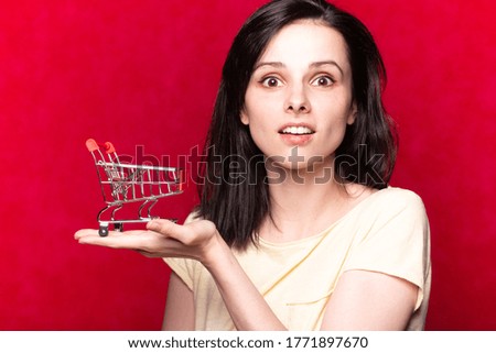 woman in yellow t-shirt holding supermarket trolley in her hands, red studio background